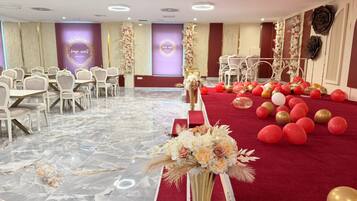 Un salón de banquetes con suelo de mármol, sillas blancas, alfombra roja y decoración floral.