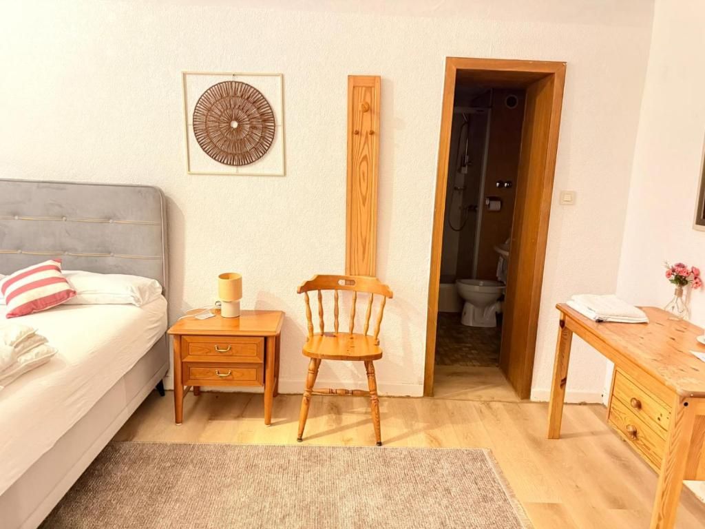 Une chambre à coucher comprenant un lit, une table de chevet, une chaise et une porte en bois donnant sur une salle de bain.