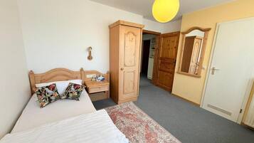A bedroom with a bed, a nightstand, a wardrobe, a mirror, and a door.