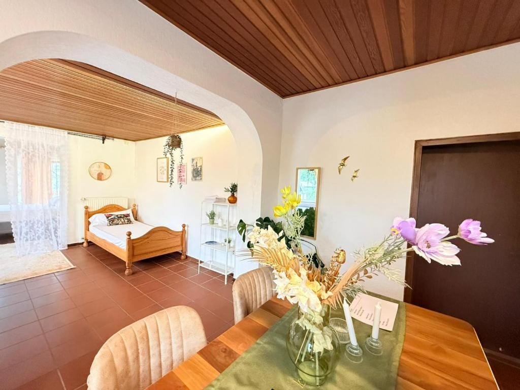 Una habitación con una cama, una mesa de comedor con un florero y un techo de madera.