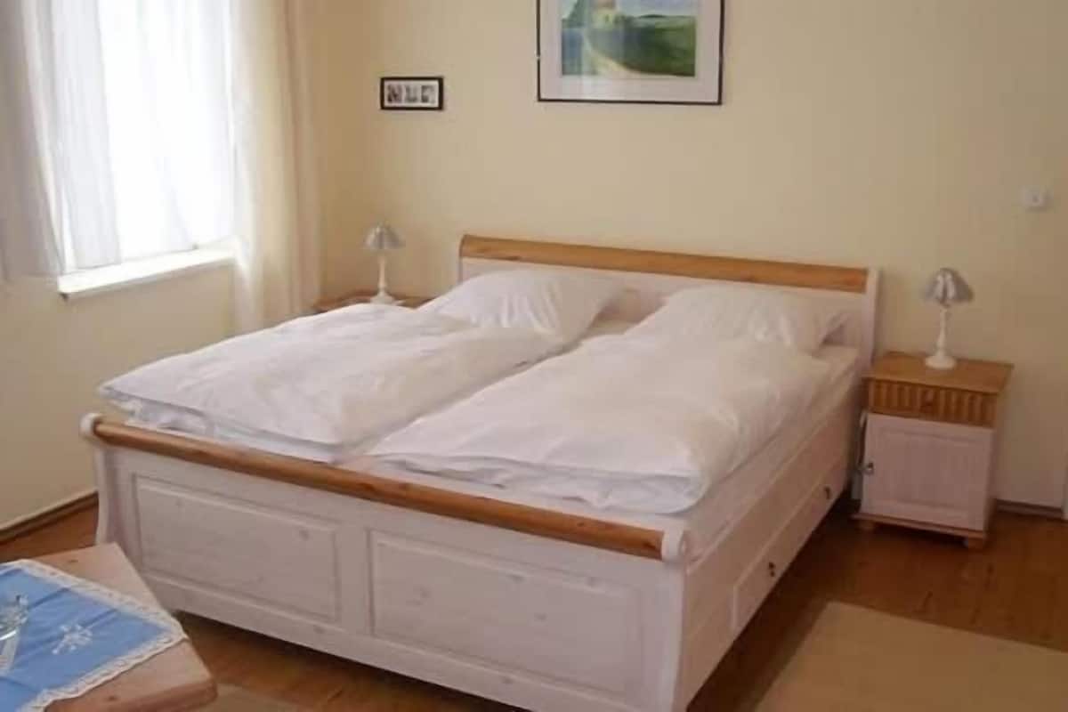 A double bed with a wooden headboard, a bedside table with a lamp, and a small cabinet.