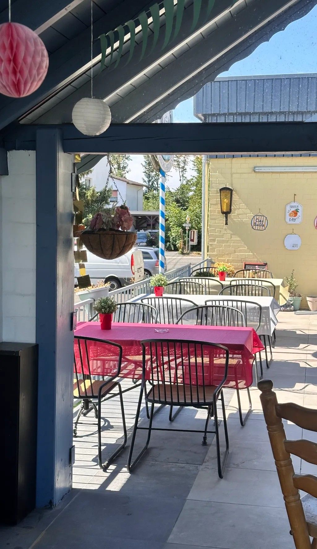An outdoor seating area with tables and chairs, a hanging flower basket, and a wall with a sign.