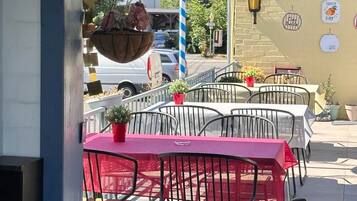 An outdoor seating area with tables and chairs, a hanging flower basket, and a wall with a sign.