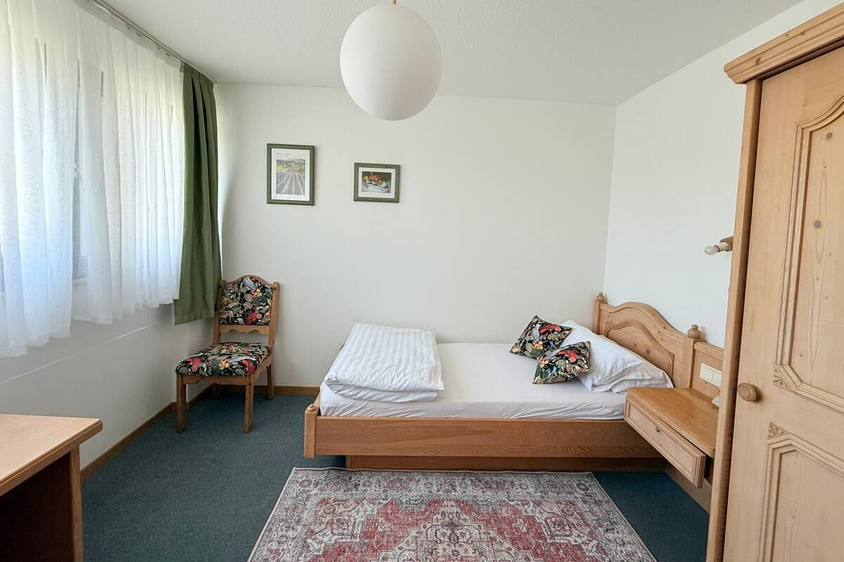 A bedroom with a wooden bed, a chair, a desk, and a wardrobe.