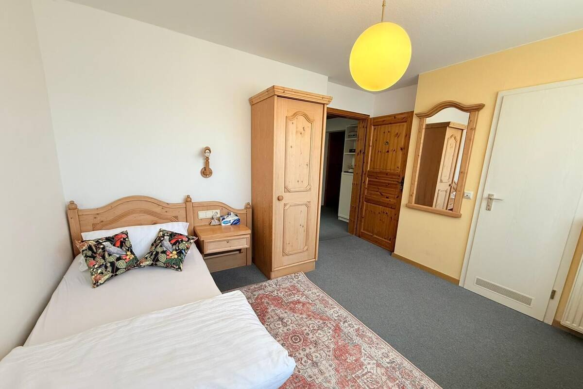 A bedroom with a bed, a nightstand, a wardrobe, a mirror, and a hanging light fixture.