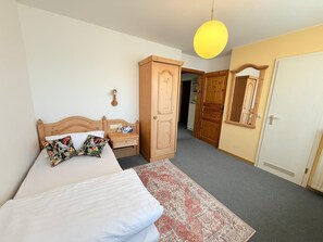 Un dormitorio con cama, mesita de noche, armario, espejo y lámpara colgante.