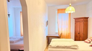 Un dormitorio con cama, escritorio, armario y una puerta que da a otra habitación.
