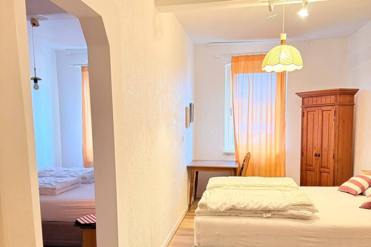 A bedroom with a bed, a desk, a wardrobe, and a door leading to another room.