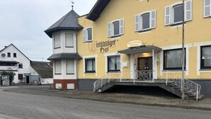 Un edificio con un cartel que dice 'Trichlögger Hof' y 'Restaurante Hotel'. Tiene una estructura tipo torre, un balcón con barandilla y una escalera que lleva a la entrada.