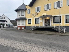 Un edificio con un cartel que dice 'Trichlögger Hof' y 'Restaurante Hotel'. Tiene una estructura tipo torre, un balcón con barandilla y una escalera que lleva a la entrada.
