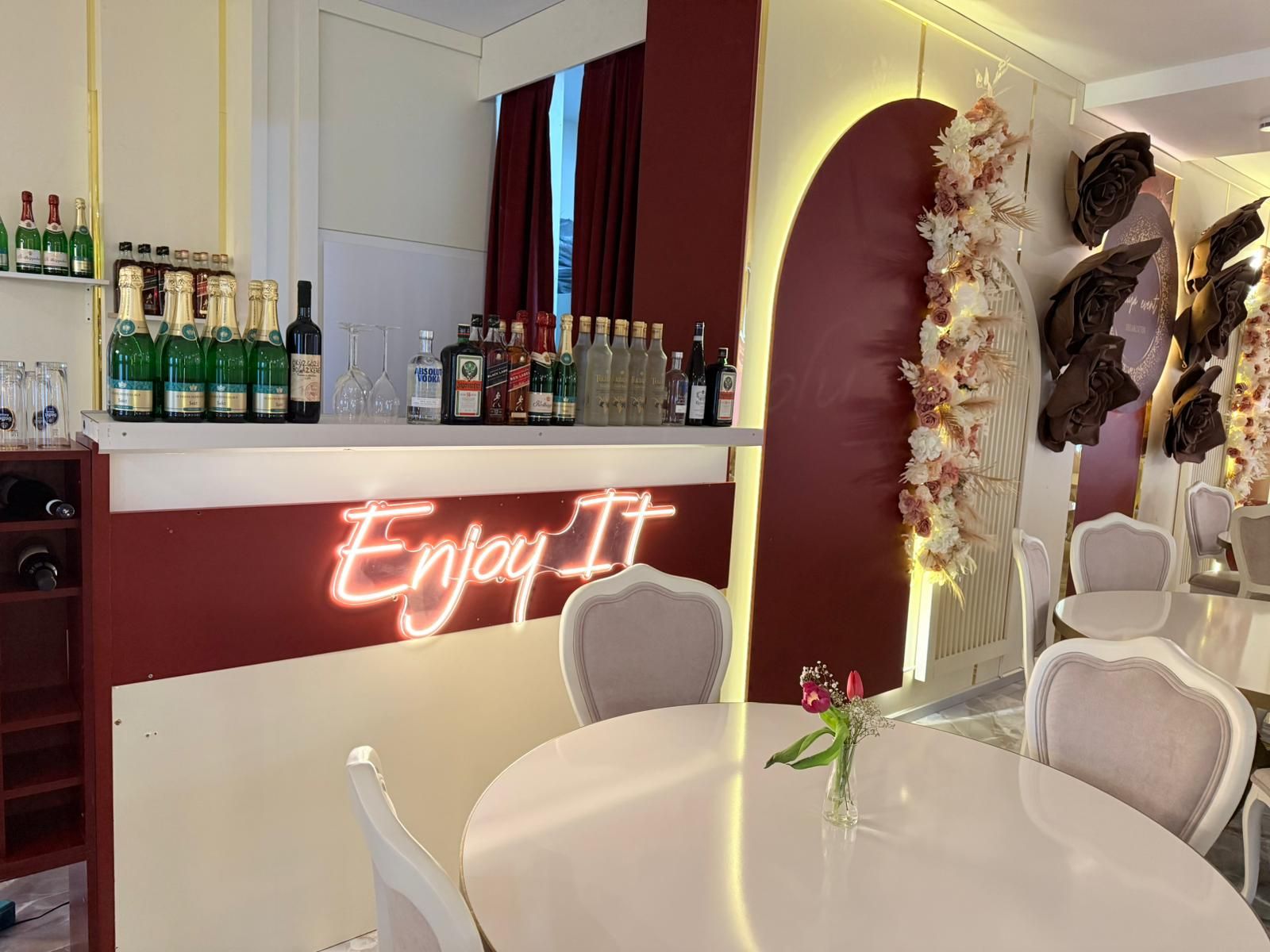 A bar area with a neon sign, a variety of bottles, and a dining area with a table and chairs.
