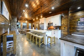 A spacious kitchen with a central island, bar stools, and a stone accent wall. - Above the Clouds · New Listing!  Scenic Views, Deck & Game Room (Broken Bow)