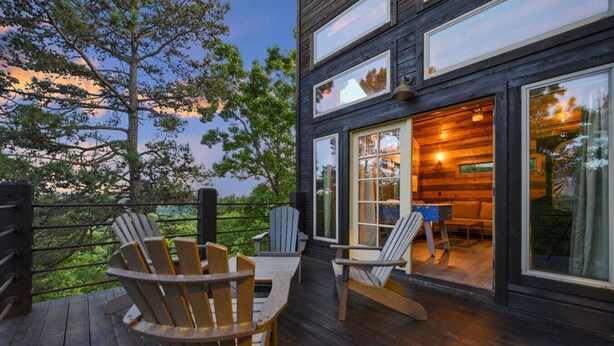 Une terrasse en bois avec des fauteuils Adirondack, une table et une vue sur l’intérieur grâce à de grandes fenêtres.