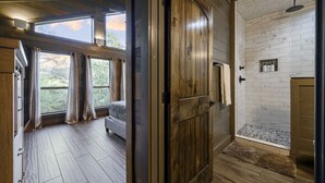 Une pièce comprenant un lit, une porte en bois et un espace douche carrelé de carreaux blancs.