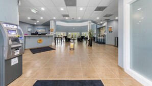 Eine Hotelhalle mit Geldautomat, Rezeption, Sitzgelegenheiten und einem großen Fenster.