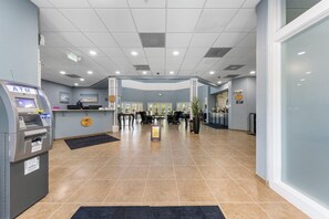 Eine Hotelhalle mit Geldautomat, Rezeption, Sitzgelegenheiten und einem großen Fenster.