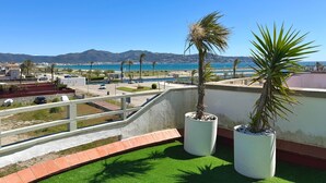 A rooftop terrace with artificial grass, two potted plants, and a view of the sea and mountains. - V002 - Cargols de Mar 2 (Empuriabrava)