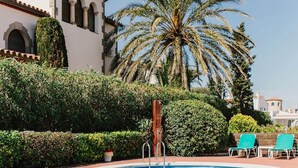 A swimming pool with lounge chairs, a palm tree, and a building with arches. - V002 - Cargols de Mar 2 (Empuriabrava)