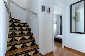 A staircase with patterned steps, a handrail, and a door leading to a room with a bed. - V036 - Joan Vinyoli 2 (Roses)