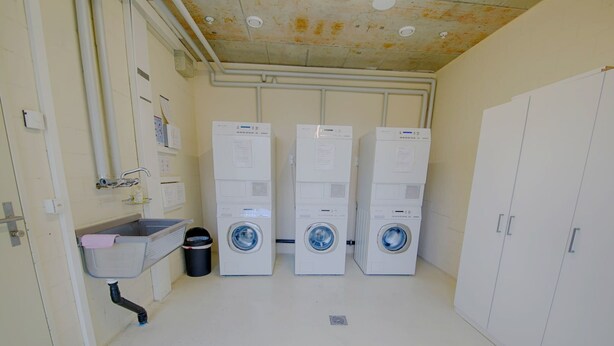 A laundry room with three stacked washing machines, a sink, and a trash can. - Apartment  by Interhome (Lucerne)