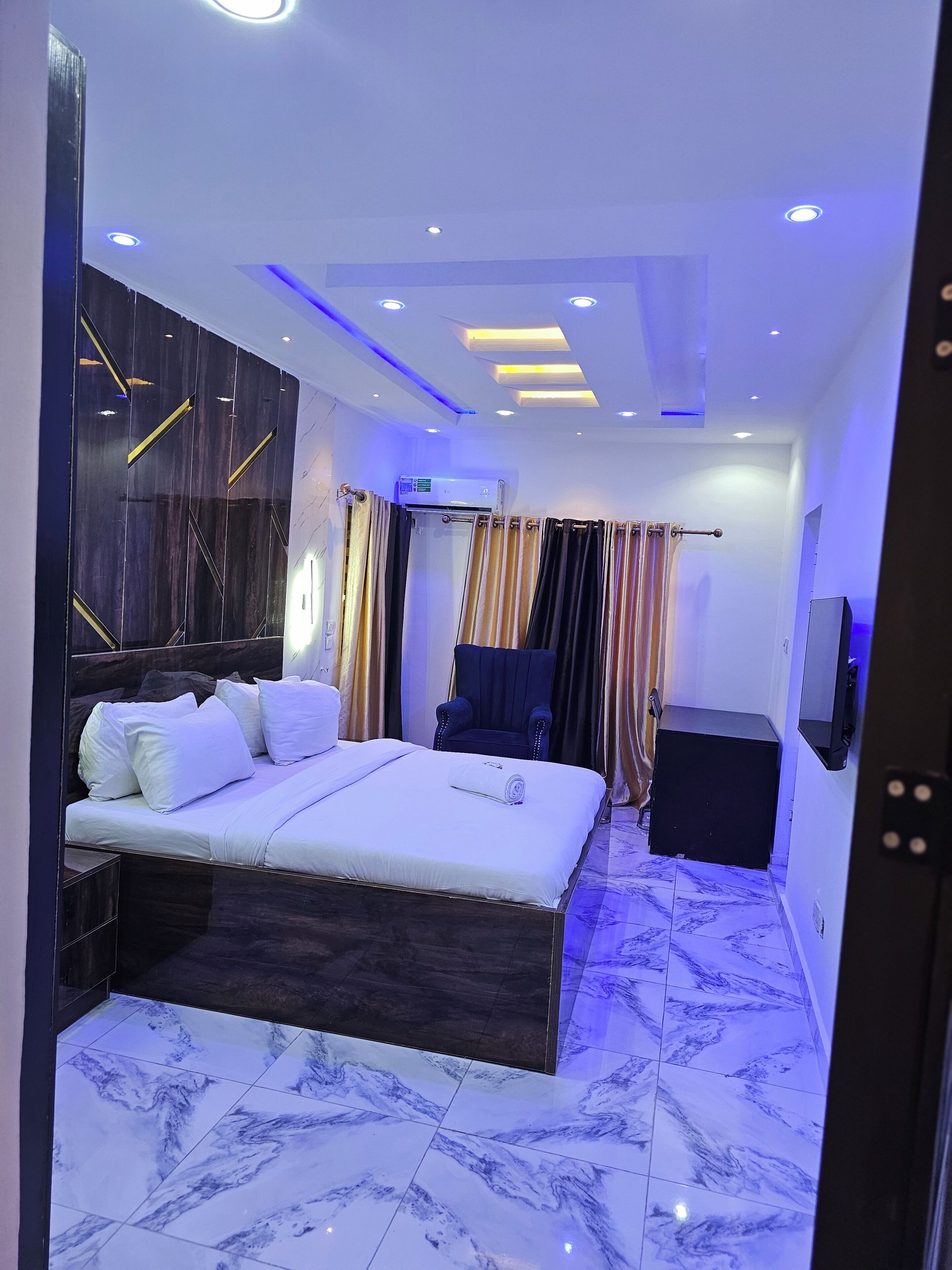A modern hotel room with a large bed, a chair, a TV, and an air conditioning unit.
