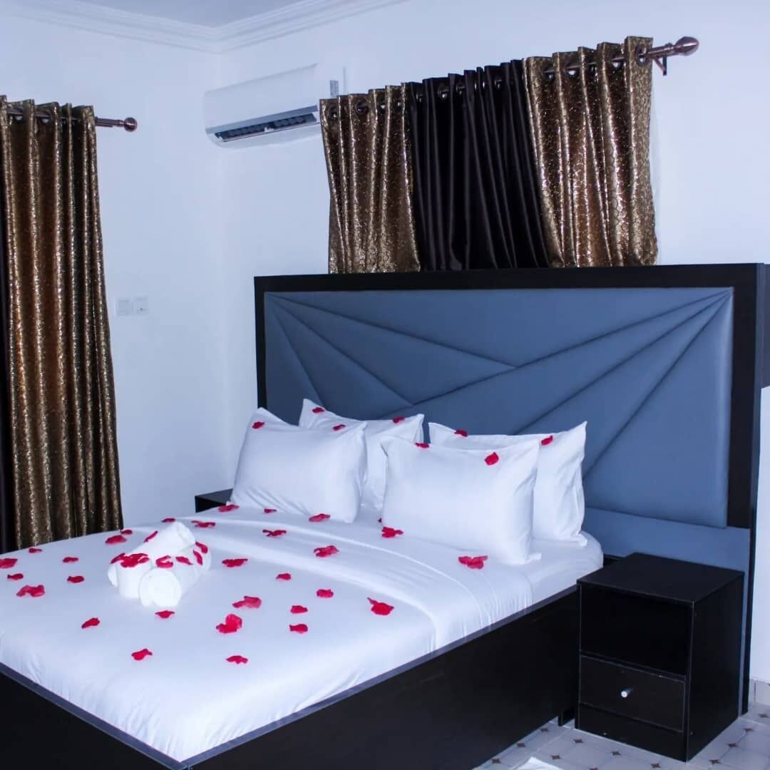 Un letto con biancheria bianca e petali di rosa, una testiera scura e un comodino nero.
