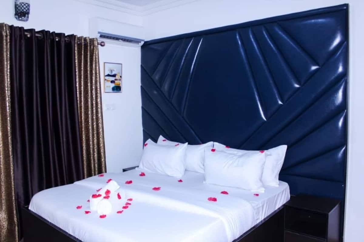 Une chambre d’hôtel avec un grand lit, une tête de lit sombre et des rideaux.