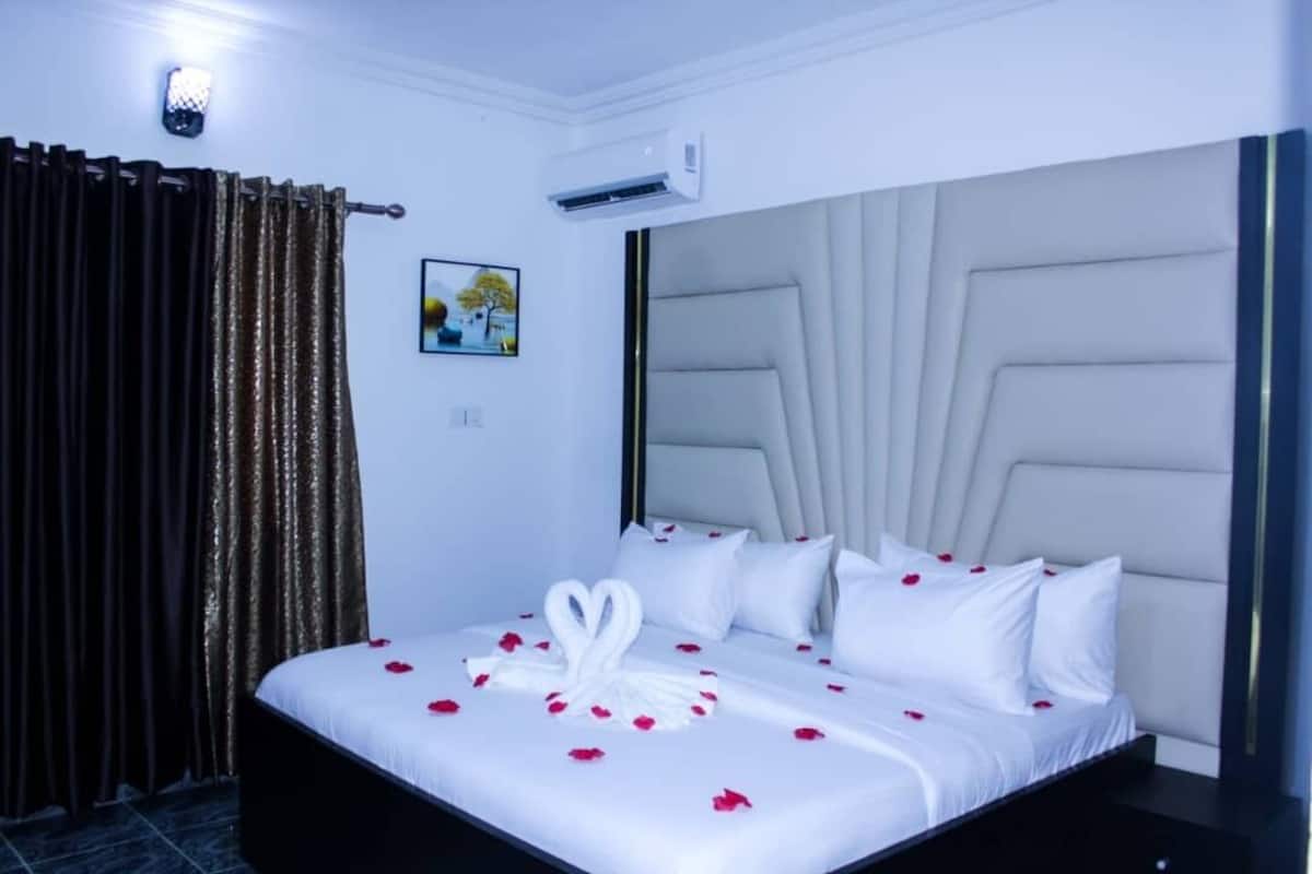 Une chambre d’hôtel avec un lit, des rideaux, un appareil de climatisation et un tableau accroché au mur.