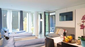 A modern hotel room with a bed, a desk, a chair, a TV, and a dining table with fruit. - LU Gletschergarten II-Allmend HITrental Apartment by Interhome (Lucerne)