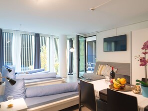 Ein modernes Hotelzimmer mit einem Bett, einem Schreibtisch, einem Sessel, einem Fernseher und einem Esstisch mit Obst.