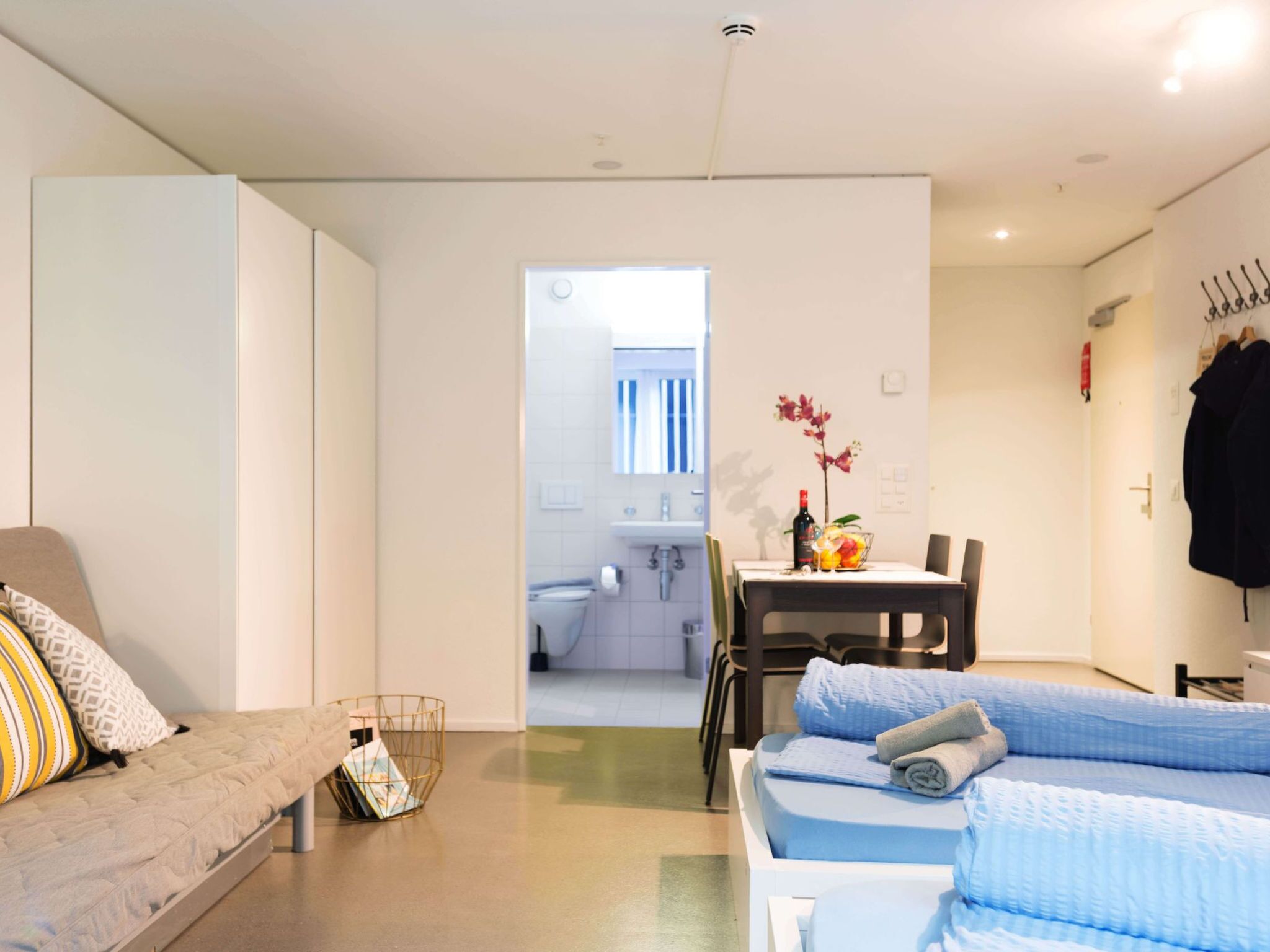 A modern, well-lit living room with a sofa, a dining table, and a view into the adjacent bathroom.