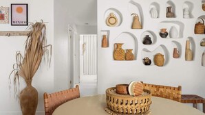 Un coin repas avec une table ronde, des paniers en osier et une variété de pièces de poterie exposées au mur.