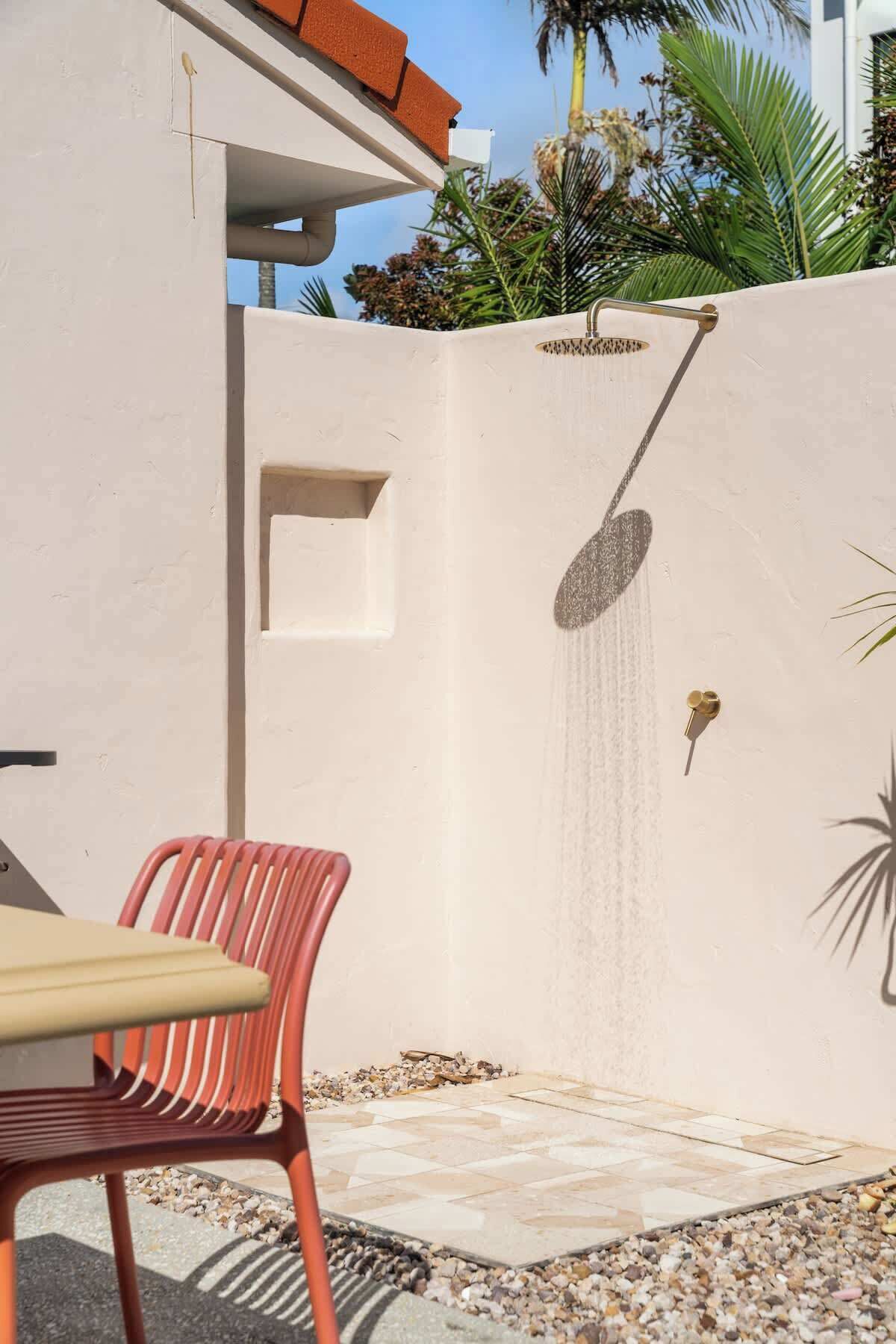 A modern outdoor shower with a rain showerhead, a red chair, and a small table.