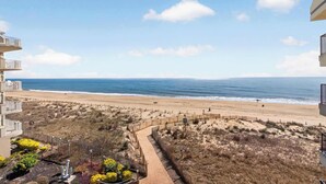 Une vue sur la plage depuis un balcon, avec un sentier sablonneux menant à la rive, une clôture et un ciel dégagé.