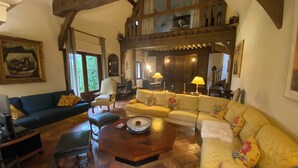 Ein traditionelles Wohnzimmer mit hohen Decken, freiliegenden Holzbalken, einer großen Sofagarnitur, einem Esstisch und einem Kamin.
