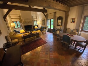 A cozy living room with a fireplace, a dining table with chairs, and a sofa. - Large Norman family home 5km from Deauville (Touques)