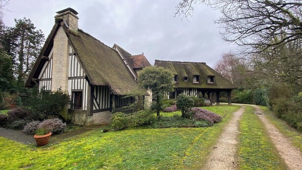 Ein traditionelles Haus mit Strohdach und einem Gartenweg, der davorführt.
