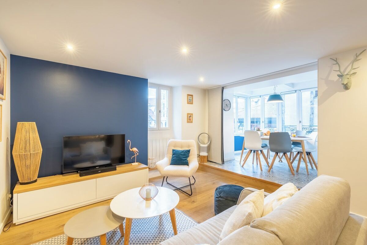 Un salon moderne doté d’un téléviseur à écran plat, d’un canapé blanc, d’une table basse ronde et d’un coin repas avec une table et des chaises.
