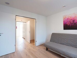 Ein Zimmer mit grauem Sofa, Holzboden und einer Tür zu einem anderen Raum.