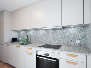 Eine moderne Küche mit weißen Schränken, einer Granit Arbeitsplatte, einer Edelstahl-Dunstabzugshaube und einem eingebauten Ofen.