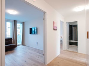 Amplia habitación con suelo de madera, un sofá, un televisor de pantalla plana y una puerta que da a un baño.