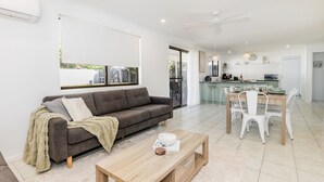 A modern living room with a sofa, coffee table, and dining area. - Anchor and Palms boat parking, pet friendly air con free wifi - walk to beach & cafes (Agnes Water)