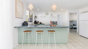 A modern kitchen with a central island, bar stools, pendant lighting, and a view into the adjacent bedroom. - Anchor and Palms boat parking, pet friendly air con free wifi - walk to beach & cafes (Agnes Water)