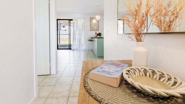 A modern kitchen with a view to the outdoors, a dining area with a book and bread basket, and a vase with dried flowers. - Anchor and Palms boat parking, pet friendly air con free wifi - walk to beach & cafes (Agnes Water)