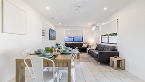 A modern living space with a dining area, a sofa, and a view of the outdoors. - Anchor and Palms boat parking, pet friendly air con free wifi - walk to beach & cafes (Agnes Water)