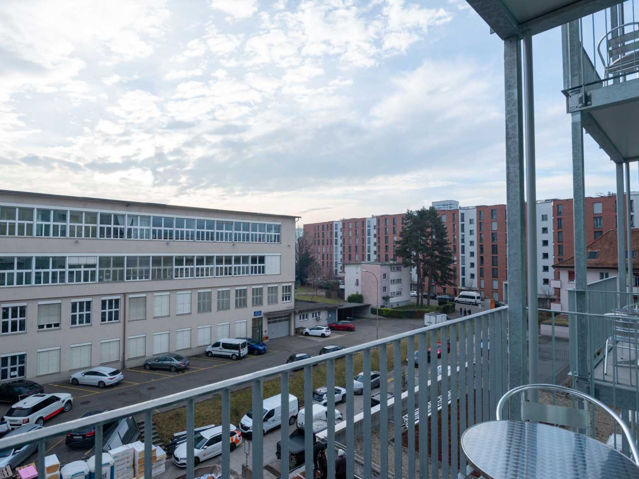 A view of a parking lot with multiple cars, a building with a flat facade, and a clear sky.