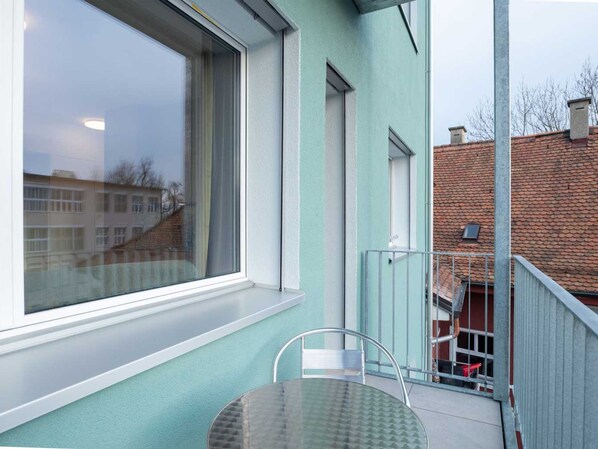 A balcony with a glass table and chairs, a large window, and a view of a building with a red roof. - ZH Red 3 - Letzigrund HITrental Apartment by Interhome (Zurich)