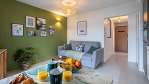 A living room with a sofa, a dining table with breakfast items, and a green wall with framed pictures. - LakeView 1 - Premium Annecy - Veyrier du lac (Veyrier-du-Lac)