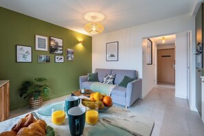 Ein Wohnzimmer mit einer Couch, einem Esstisch mit Frühstücksgebäck und einer grünen Wand mit gerahmten Bildern.