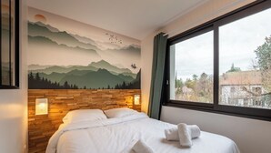 A hotel room with a bed, a mural of mountains, a wooden headboard, and a window with a view. - LakeView 1 - Premium Annecy - Veyrier du lac (Veyrier-du-Lac)